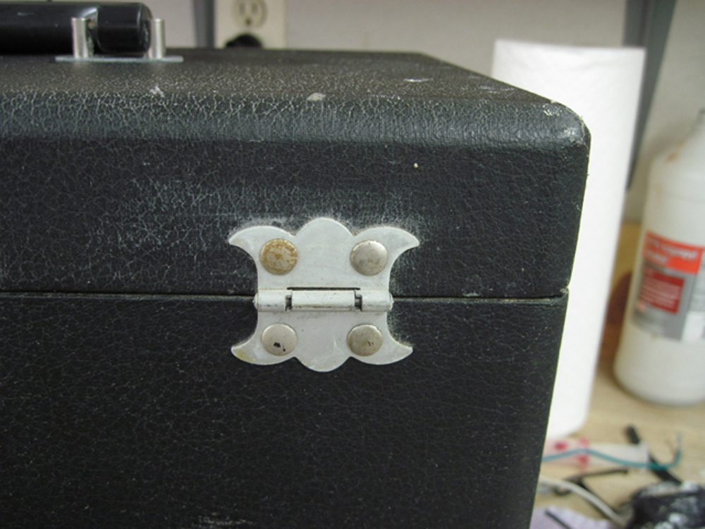 A closeup of the rear hinge before restoration. The metal is dull and the four large rivets are slightly rusty.