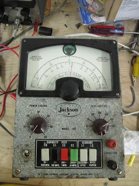 A view of the front panel with colored capacity test buttons, gray leakage test buttons, a power factor knob, a test voltage knob, a power switch, and test lead lugs.